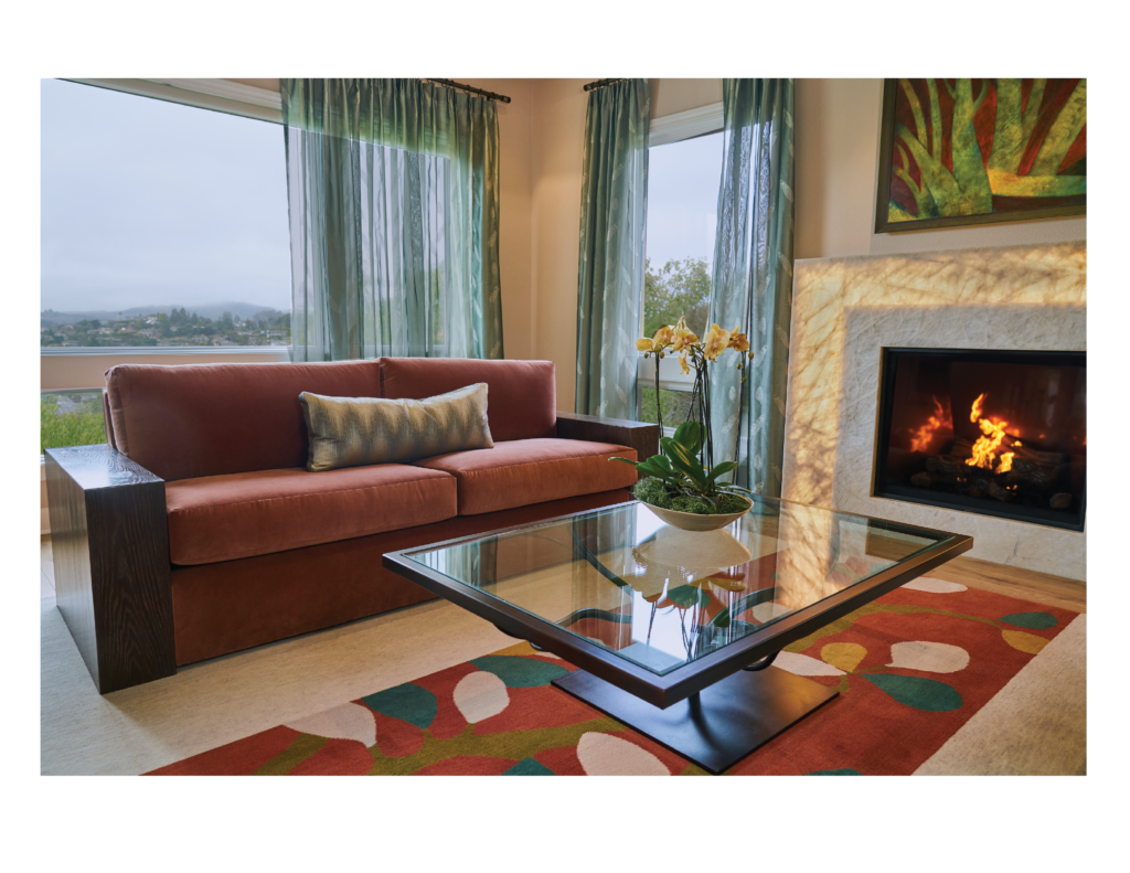 Luxury interior design for a home in Tiburon, California, in the San Francisco Bay Area, including custom designed and upholstered furniture by Ruth Livingston Designs. 

The room includes a custom designed and upholstered sofa in a living room with a fireplace, glass coffee table, rug, drapes, and fine art. 